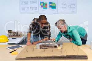 Male and female architects discussing over model structure of house at desk