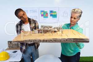 Male and female architects looking at model structure of house