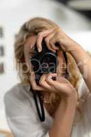 Female graphic designer clicking pictures with digital camera in office