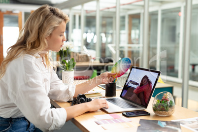 Female graphic designer looking at color swatch while using laptop at desk