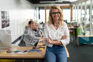 Female graphic designer sitting with arms crossed at desk in office