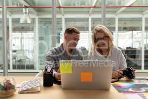 Male and female graphic designers discussing over laptop at desk