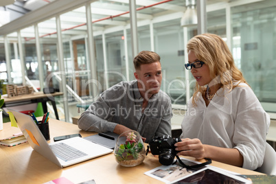 Male and female graphic designers discussing over digital camera at desk