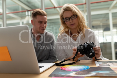 Male and female graphic designers discussing over digital camera at desk