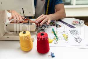 Male fashion designer using sewing machine on a table in design studio