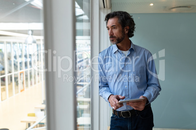 Businessman with digital tablet looking through window in office