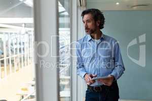 Businessman with digital tablet looking through window in office