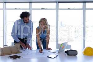 Male and female architect working on blueprint at table in modern office