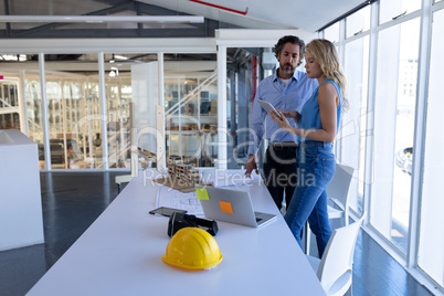 Male and female architect discussing over digital tablet at table in modern office