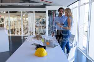 Male and female architect discussing over digital tablet at table in modern office