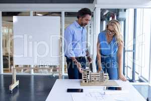 Male and female architect discussing over architectural model at table in a modern office