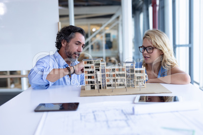 Male and female architect discussing over architectural model at table in a modern office