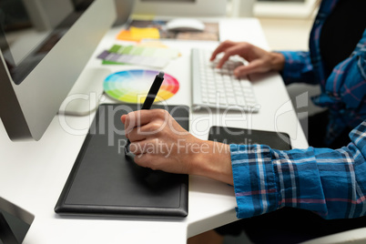 Female graphic designer using graphic tablet at desk in office