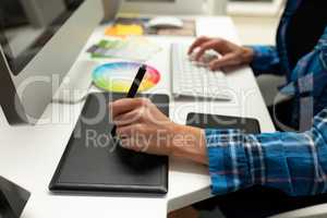 Female graphic designer using graphic tablet at desk in office