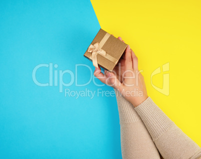 women's hands hold a closed box with a bow on a blue-yellow back