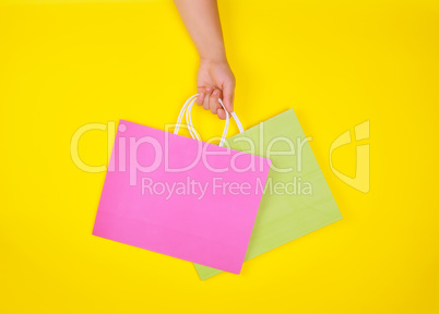 hand holding two paper shopping bags on a yellow background