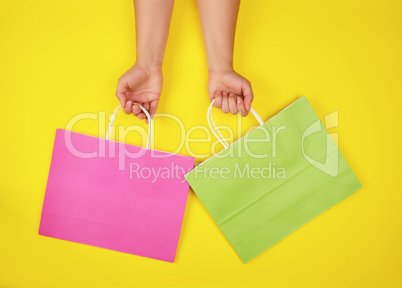 two hands holding paper shopping bags on a yellow background