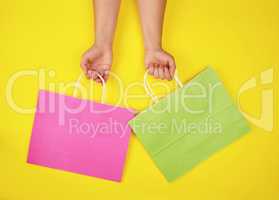 two hands holding paper shopping bags on a yellow background