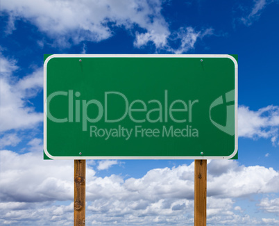 Blank Green Road Sign with Wooden Posts Over Blue Sky and Clouds