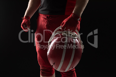 American football player standing with helmet against black background