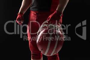 American football player standing with helmet against black background