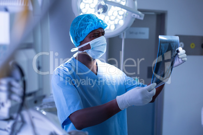 Male surgeon with surgical mask examining x-ray in operating room at hospital