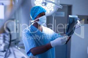 Male surgeon with surgical mask examining x-ray in operating room at hospital