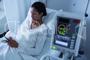 Female patient using mobile phone while relaxing on bed