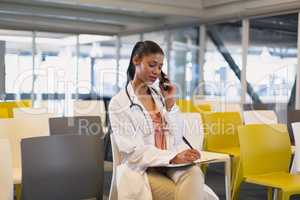 Female doctor talking on mobile phone while writing on a clipboard