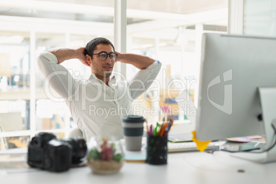 Male graphic designer sitting with hands behind hand at desk