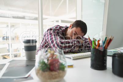 Male graphic designer sleeping on desk in office