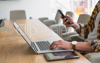 Male executive using mobile phone while working on laptop in the conference room at office