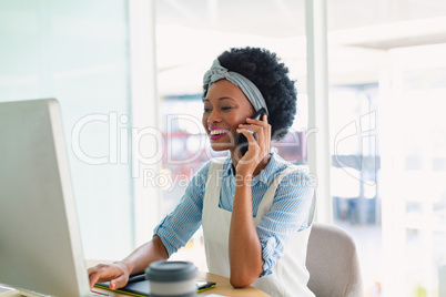 Female graphic designer talking on mobile phone at desk