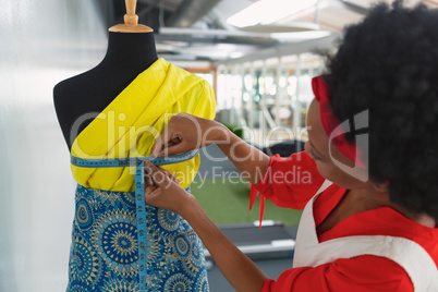 Female fashion designer using measuring tape on a mannequin in studio