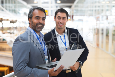 Businessmen looking at camera while working on laptop in a modern office