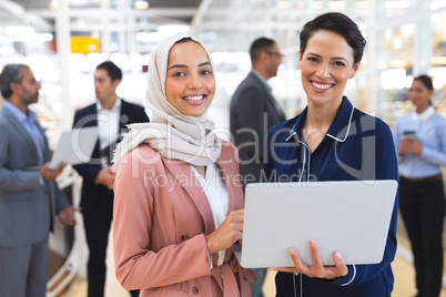 Businesswomen looking at camera while working on laptop in a modern office