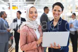 Businesswomen looking at camera while working on laptop in a modern office