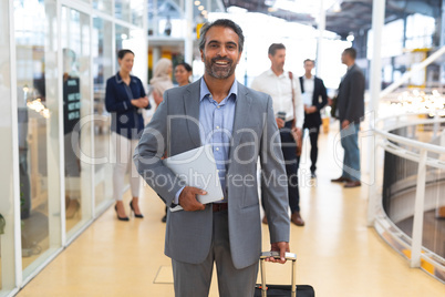 Businessman holding laptop and trolley bag and looking at camera in a modern office
