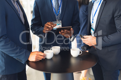 Business people discussing over digital tablet while having coffee in office