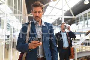 Businessman using mobile phone while walking in the corridor