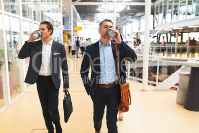 Businessmen having coffee while walking together in the corridor at office