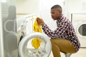 Man putting clothes in washing machine in kitchen at home
