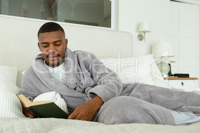 Man reading a book while lying on bed in bedroom at comfortable home