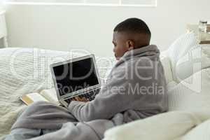 Man using laptop while lying on bed in bedroom at comfortable home