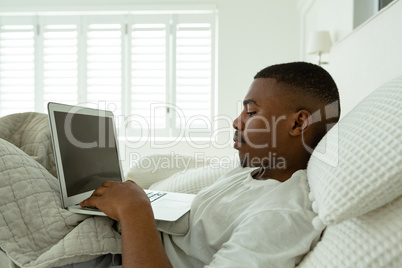 Man using laptop while lying on bed in bedroom at comfortable home