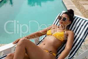 Woman in bikini relaxing on a sun lounger near swimming pool