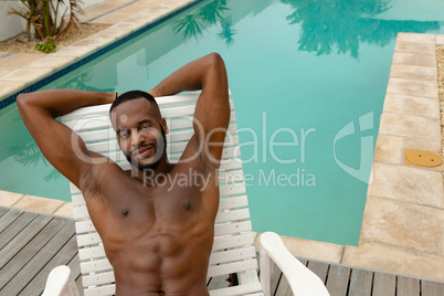 Man looking at camera while relaxing on a sun lounger near swimming pool at the backyard of home