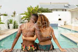 Couple sitting together near swimming pool at the backyard of home