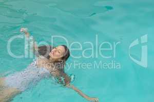 Woman with eyes closed floating in swimming pool at the backyard of home