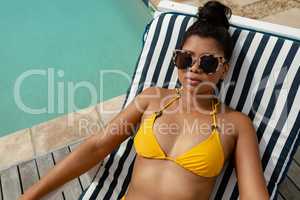 Woman in bikini relaxing on a sun lounger near swimming pool